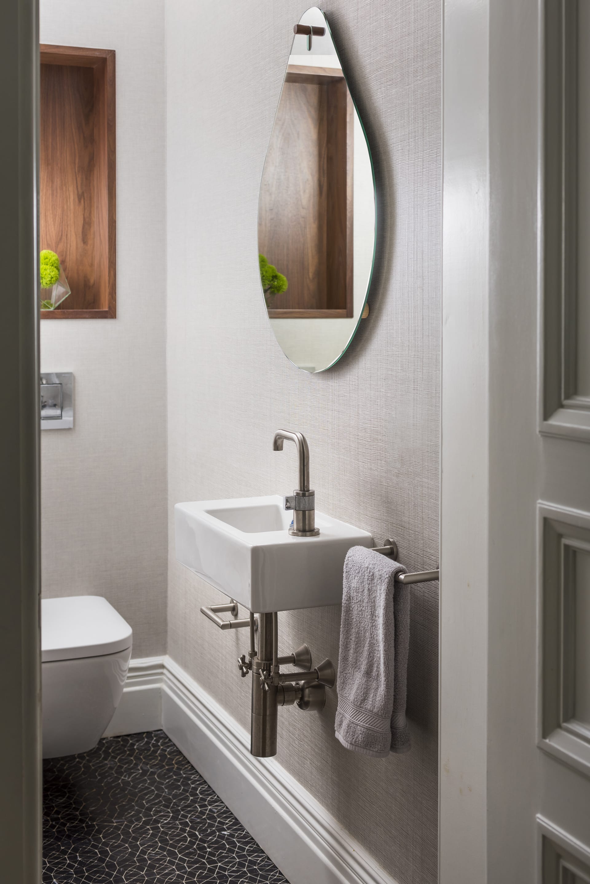Powder room with a teardrop shaped mirror, wooden niche, and textured tan wallpaper