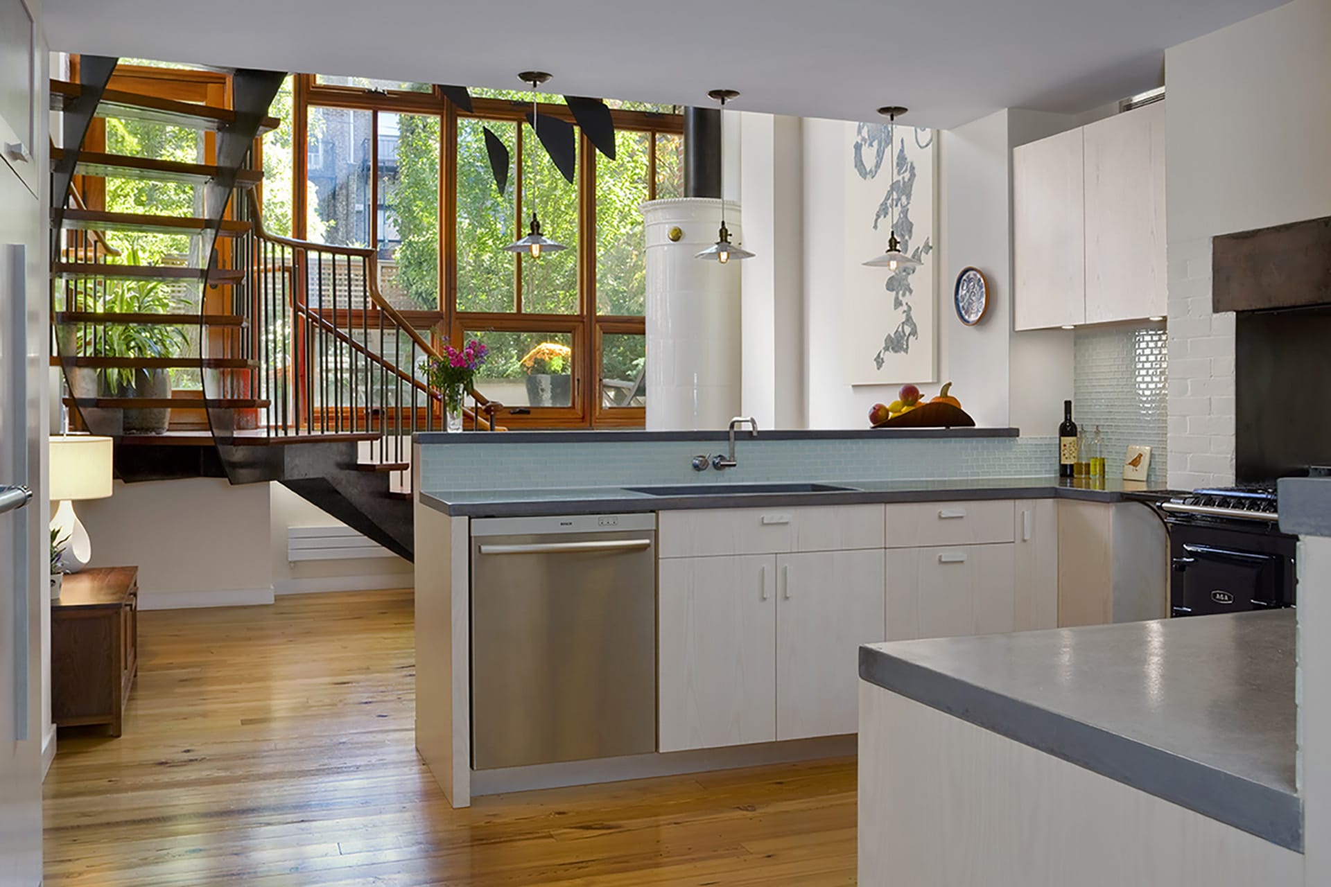 View from kitchen with light washed wood cabinets looking back to an open staircase and floor-to-ceiling windows looking out to the rear yard.