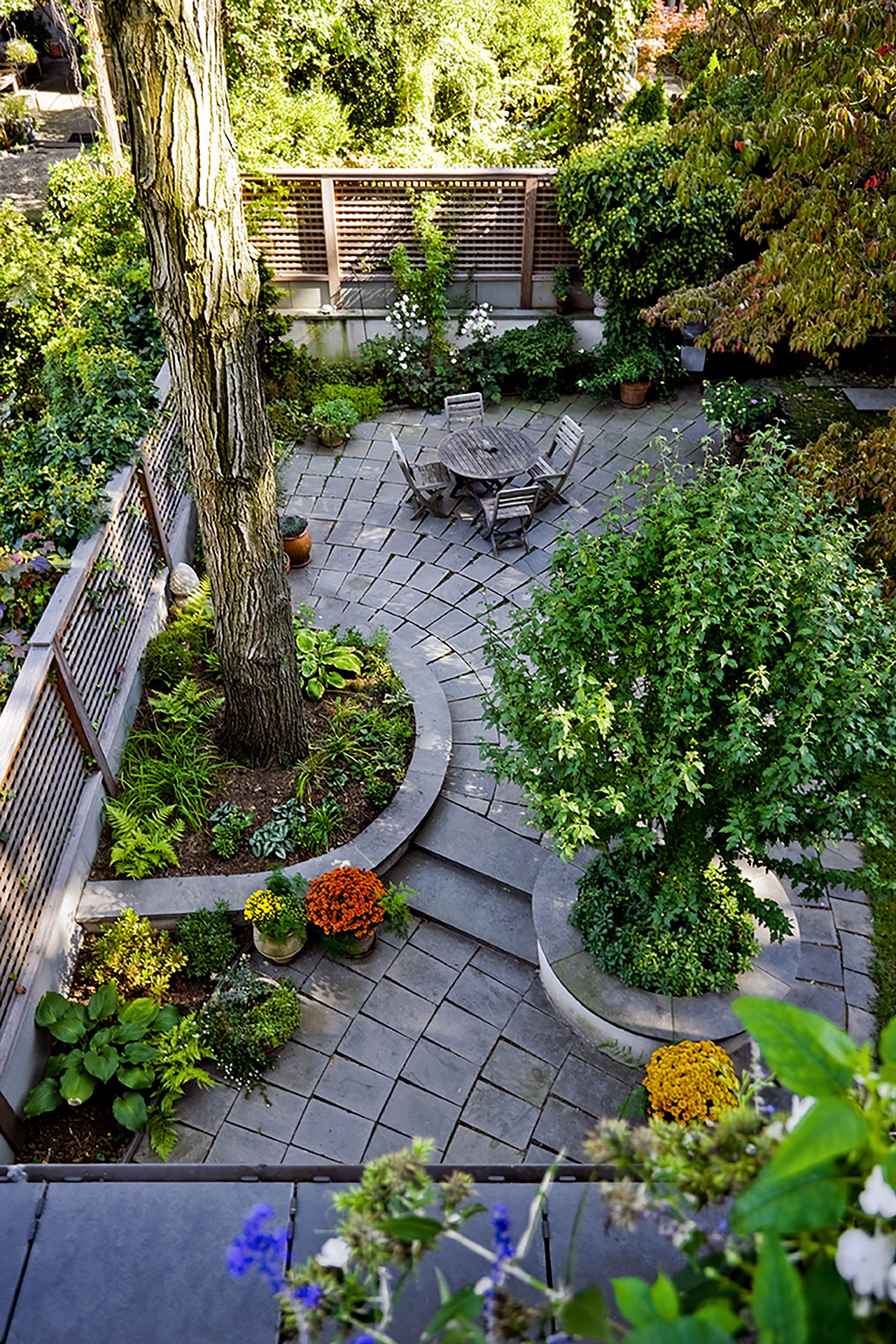 Rear yard with one large tree, lots of flowers and landscaping, and winding stone pavers throughout.