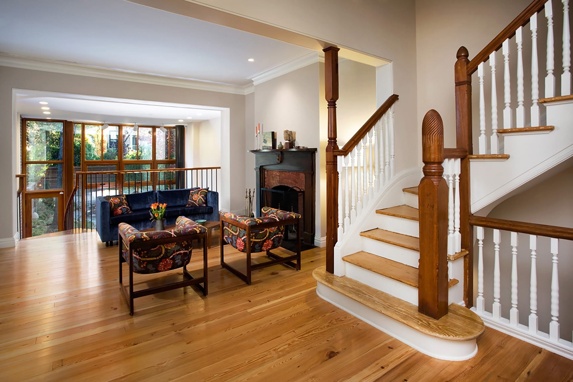 Parlor level seating area with blue velvet couch, velvet chairs, and a wood staircase leading upstairs.