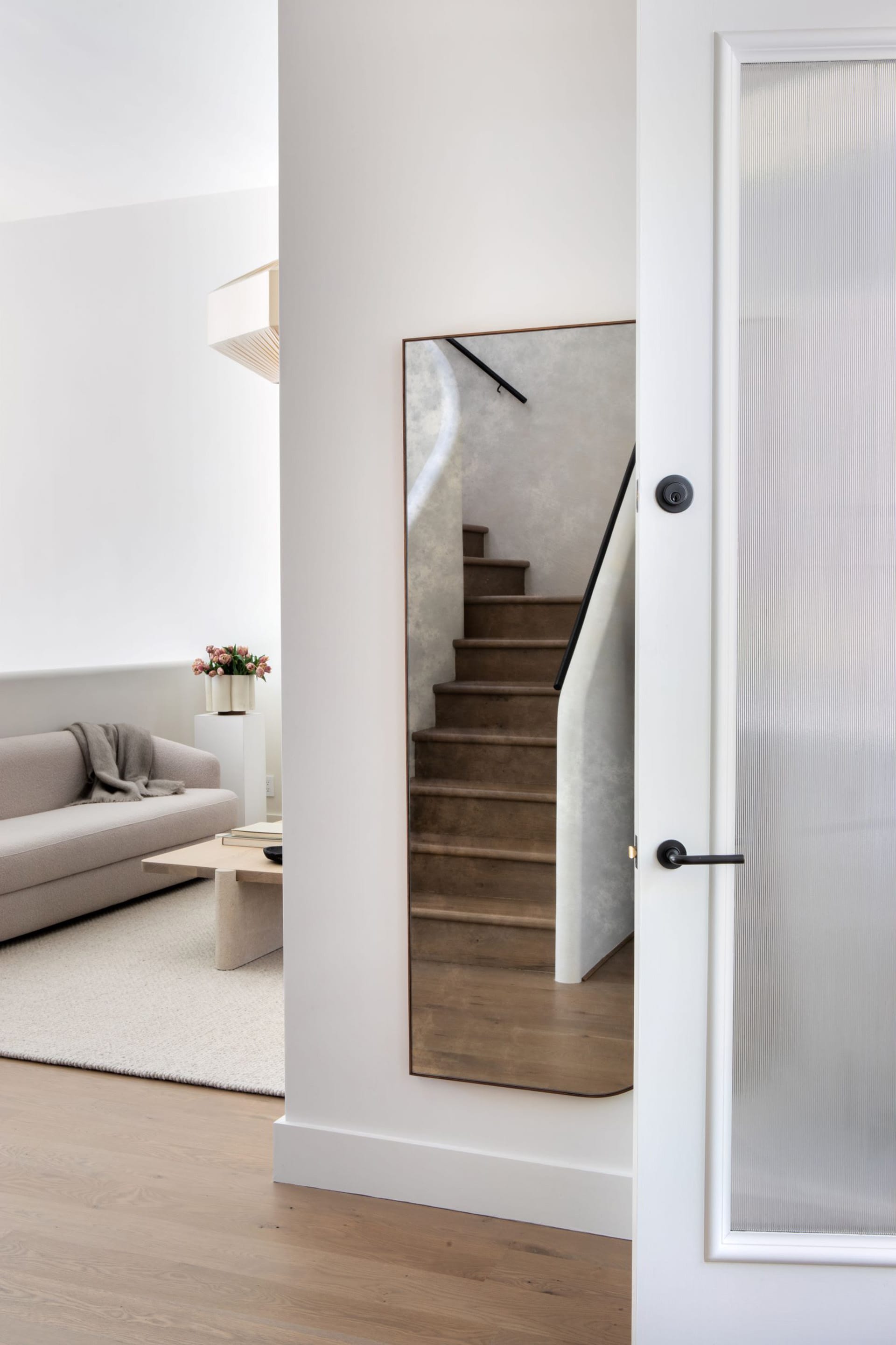 Weathered mirror in an entryway reflects a wood-floored plaster staircase.