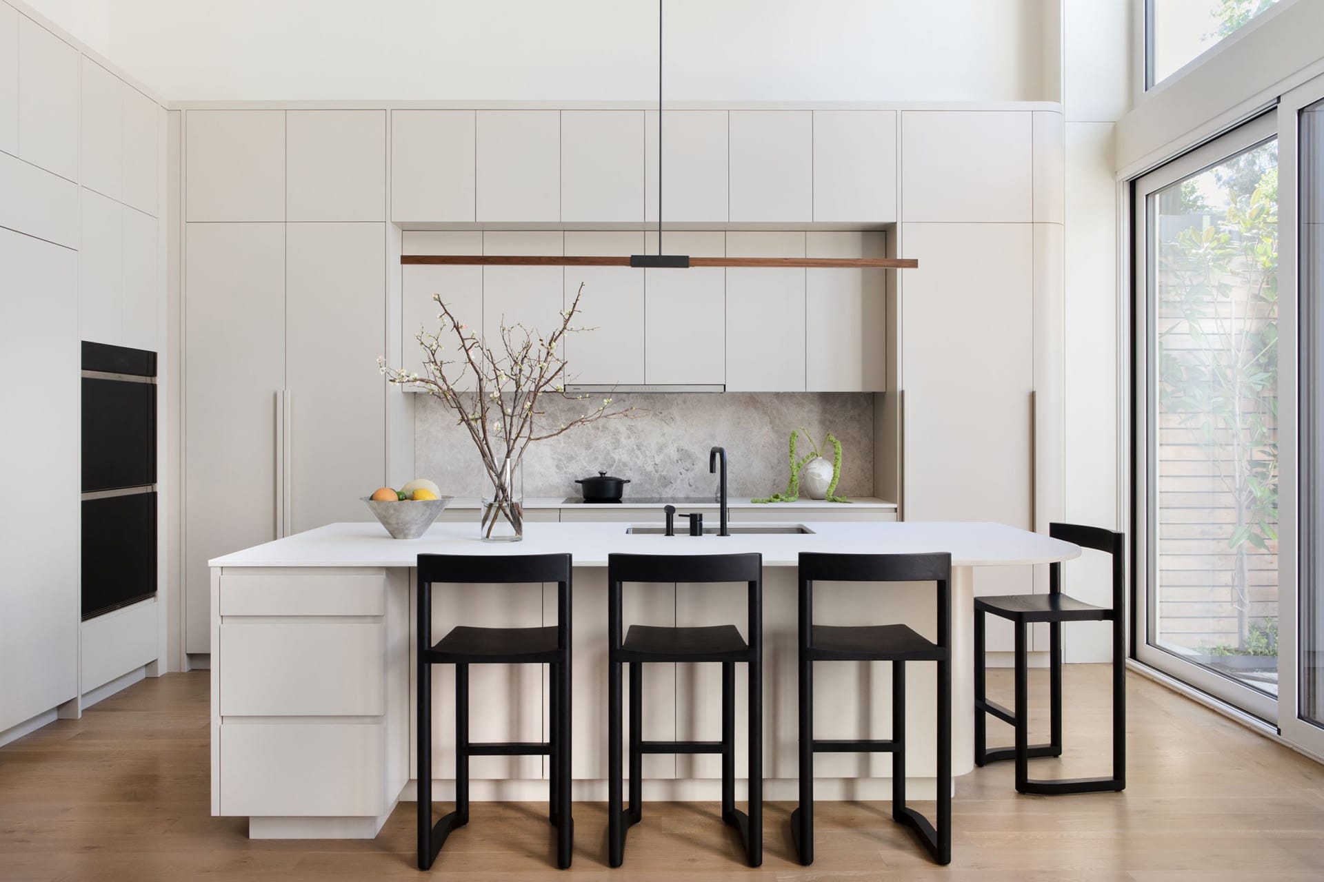 Modern kitchen with white millwork, a white countertop, marble backsplash, and four black barstools.