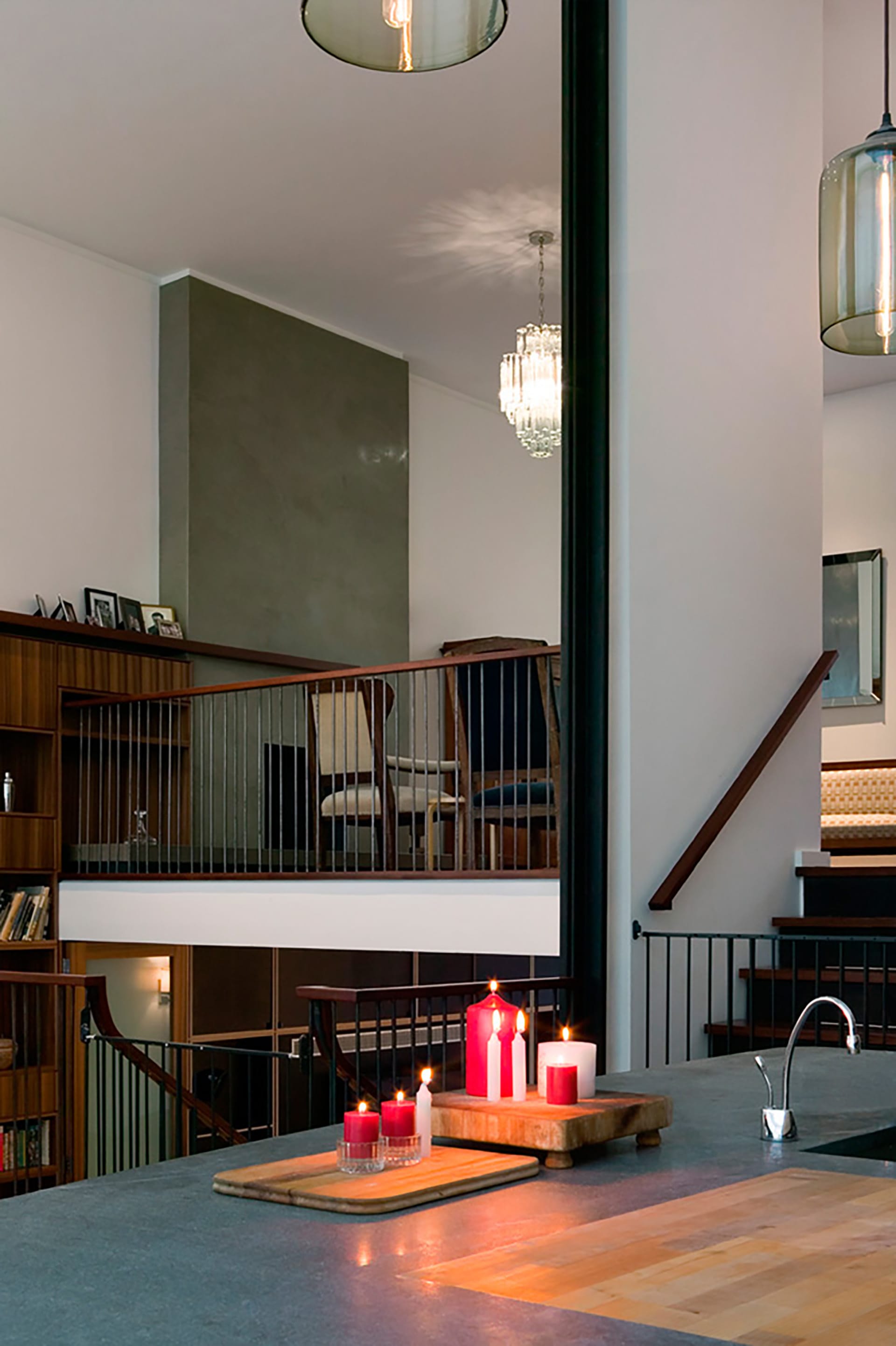 Double height space with a large grey fireplace and living room on the upper floor. The spaces are divided by dark metal balisters with wood handrails.