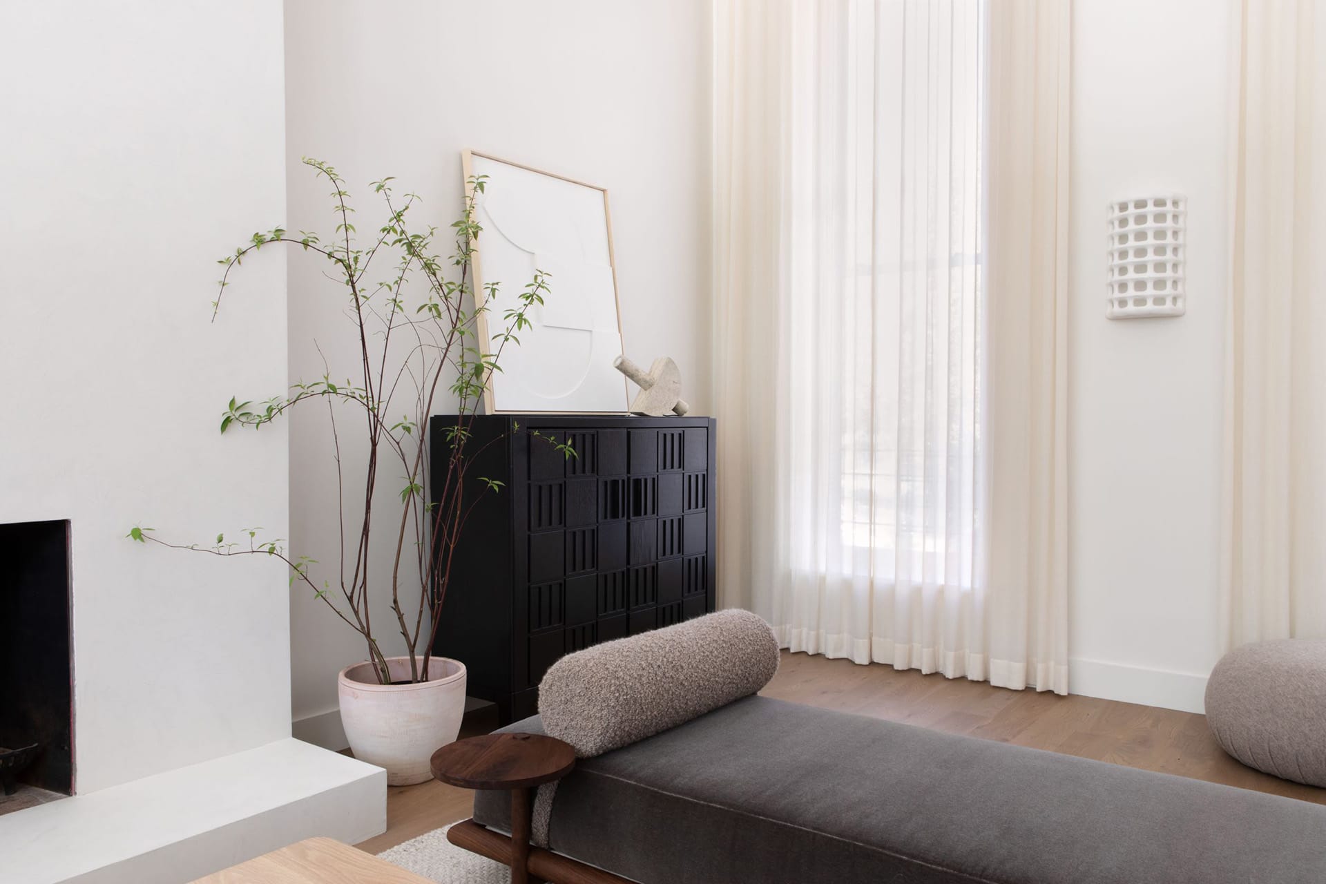 Living room with a black credenza, grey settee, and white curtains.