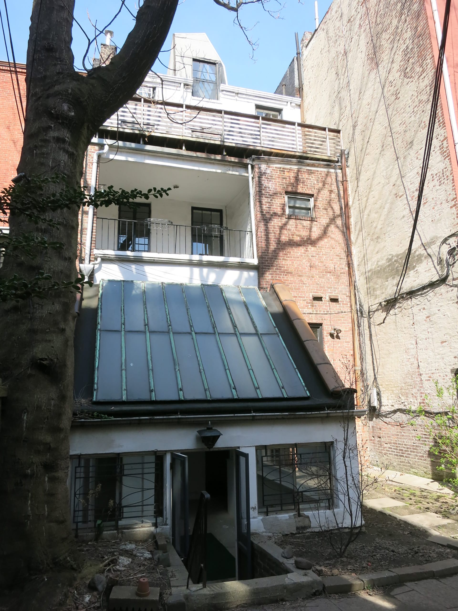 Rear facade of a Brooklyn Heights townhouse. A two story extension has a sloped glass roof. On the third floor, a balcony spans the left half of the building. The right half of the building is clad in brick.