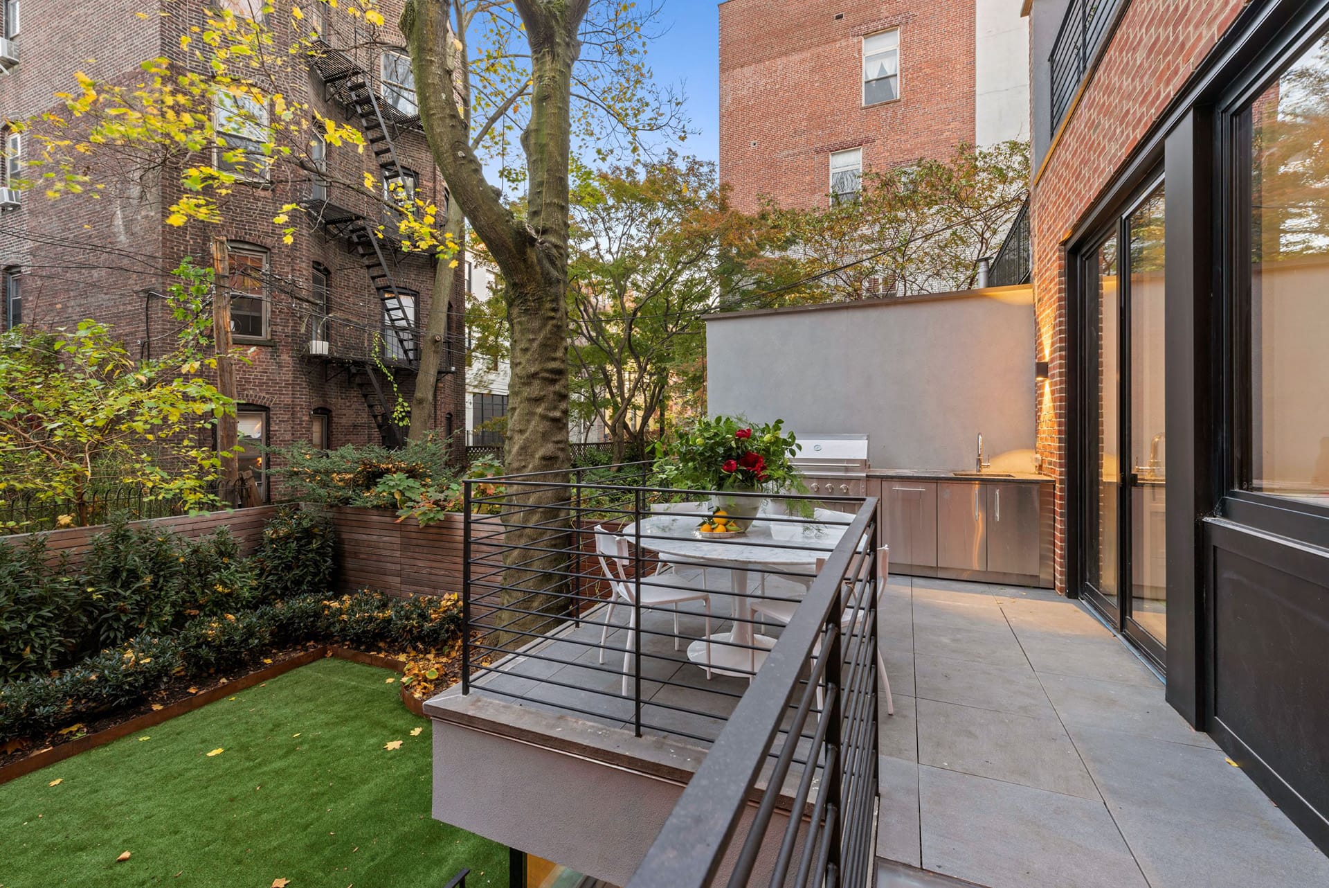 Rear patio with bluestone pavers, table and chairs, and large gas grill, overlooking a lushly landscaped rear yard.