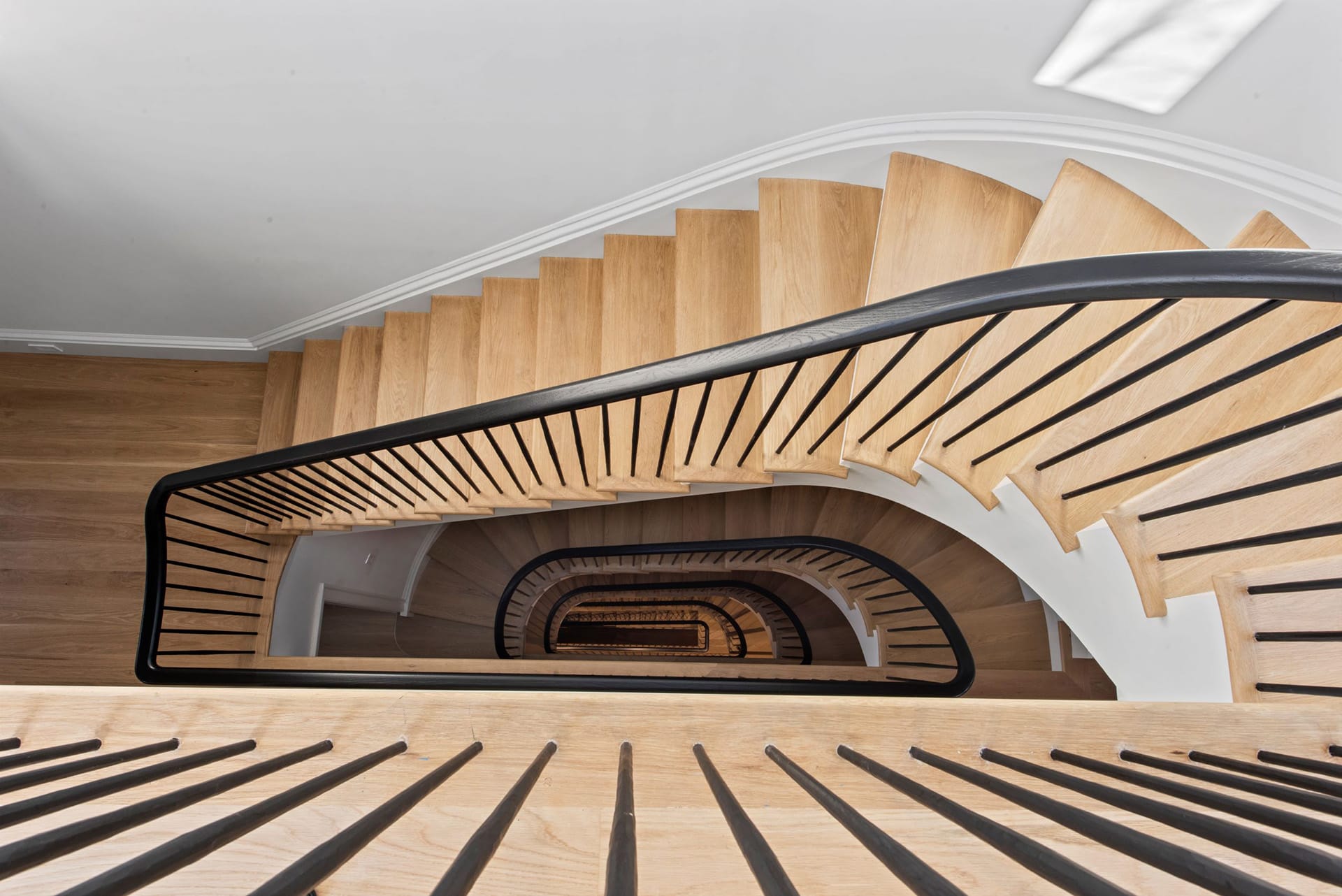 View looking down an open staircase from the fifth floor of a townhouse. The staircase has white oak risers and black handrail