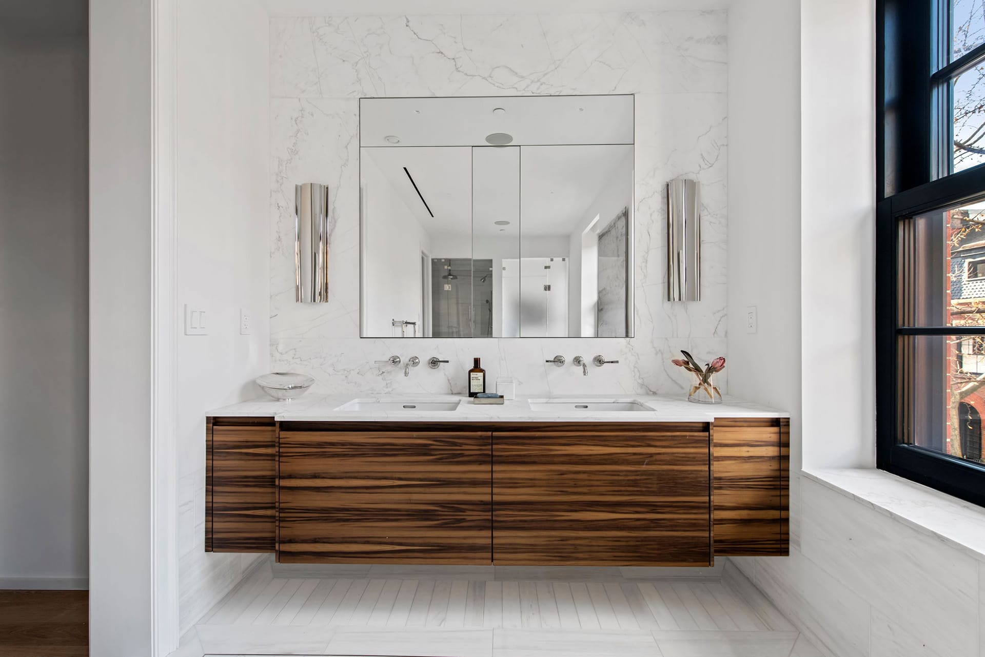 Floating wood vanity with Jack and Jill sinks, white marble countertops, and white stone tiles on the walls and floors.