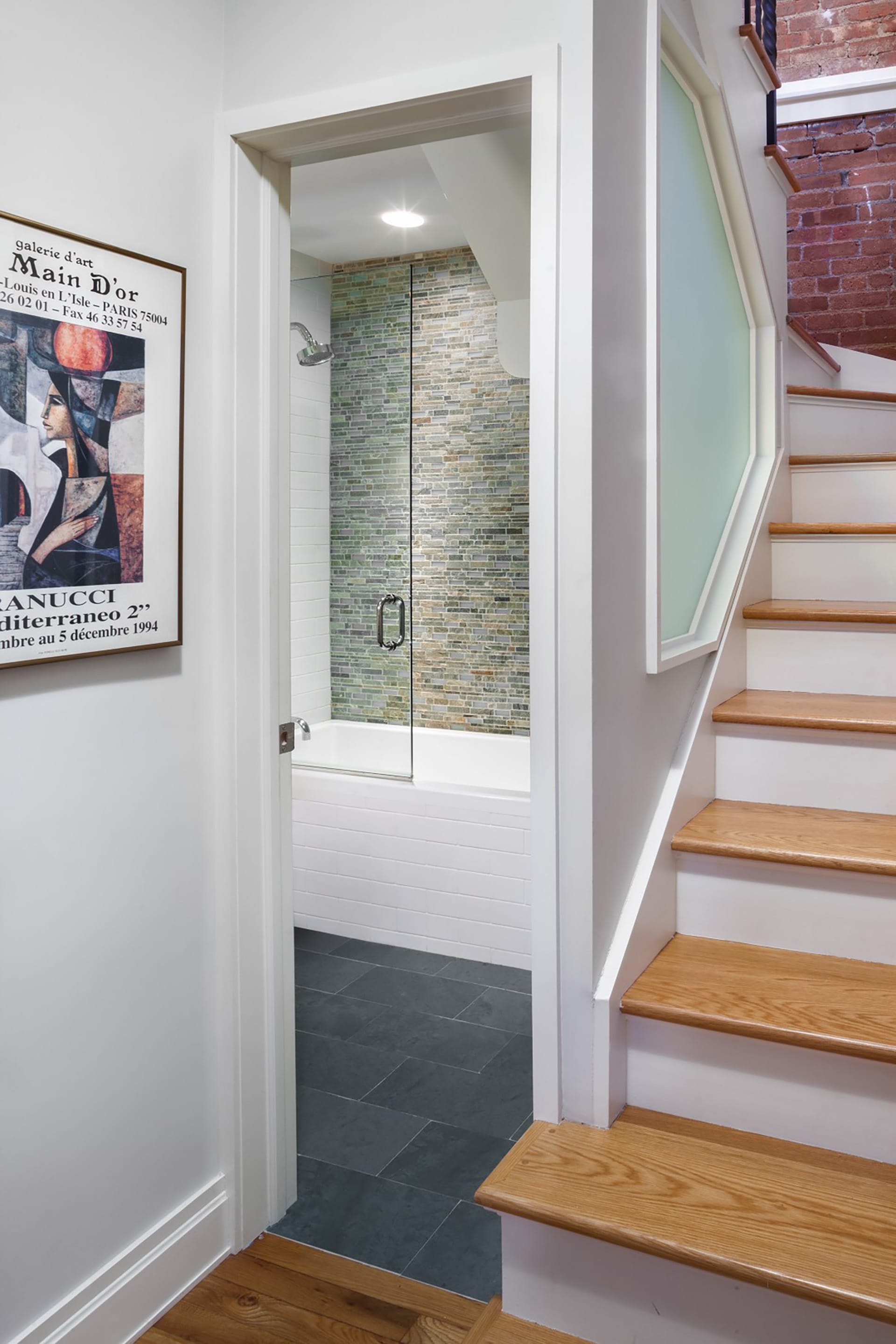 Staircase leading to the lower floor of a loft apartment next to the primary bathroom. A frosted glass wall lets light in from the stairwell to the bathroom