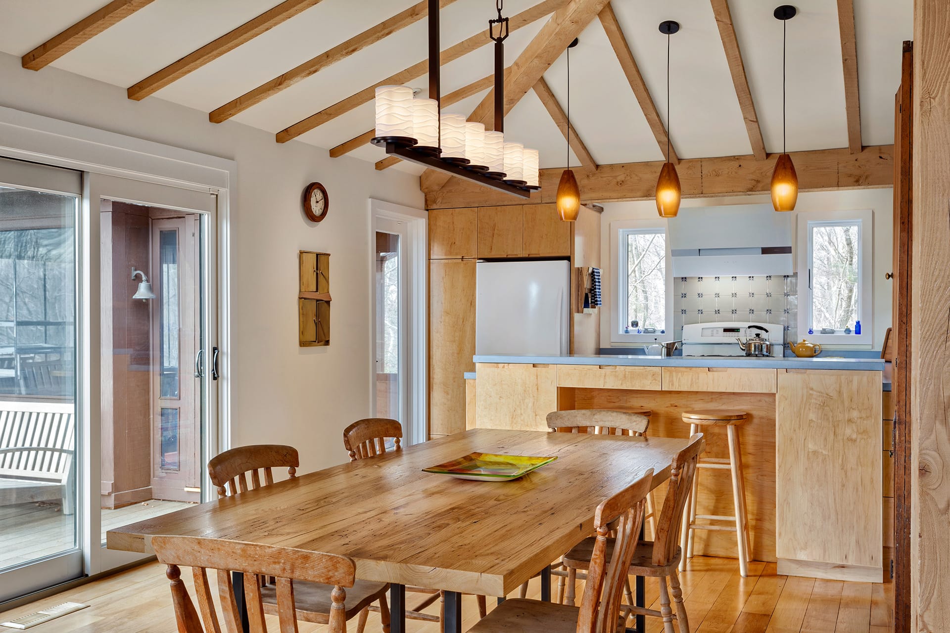Dining area in front of the kitchen in a Connecticut home. The wooden table matches the floors, cabinetry, and exposed ceiling beams.