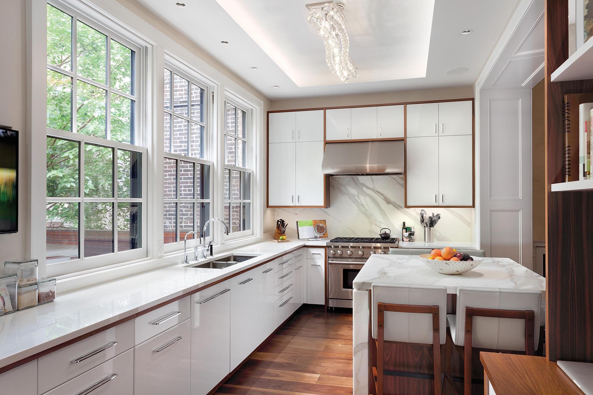 Kitchen with white cabinetry with natural wood trim, three large windows, and a white marble kitchen table