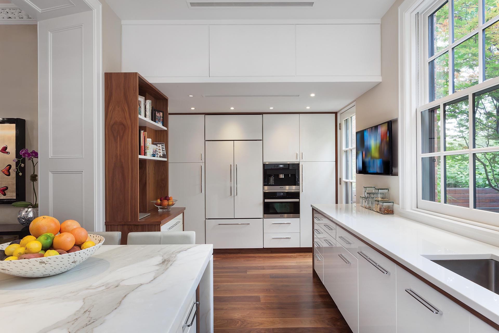 Kitchen with white cabinetry with natural wood trim, three large windows, and a white marble kitchen table