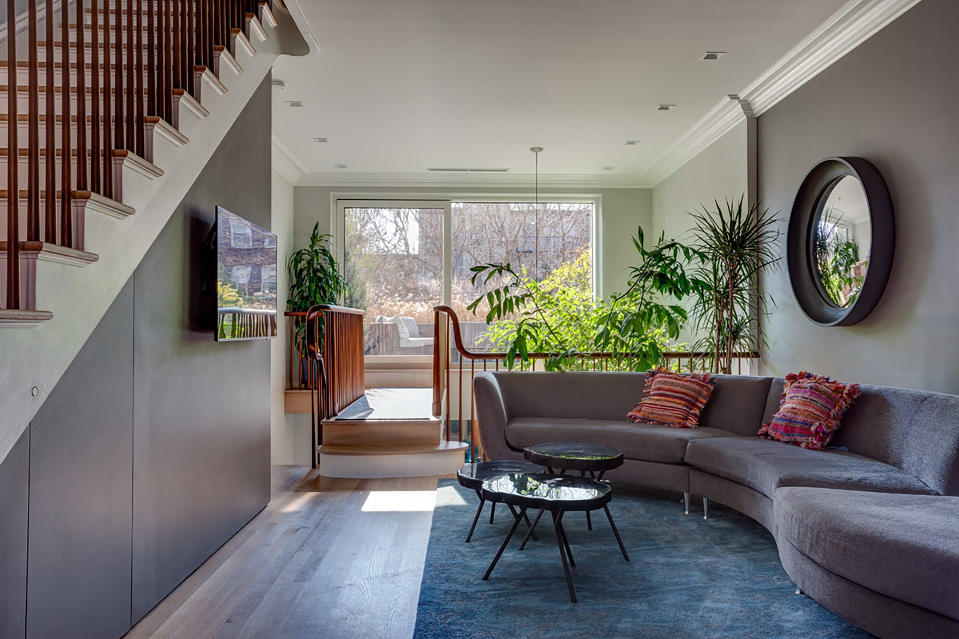 Second floor seating area with an asymmetric grey couch and walkway above a double-height space, leading to an elevated deck.