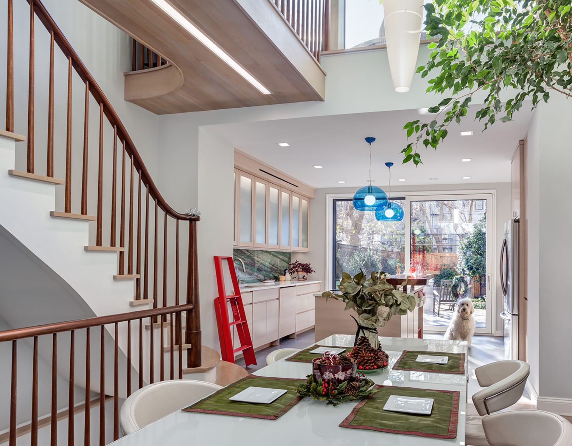 White dining room table in front of a light wood kitchen in Carroll Gardens. Two large glass doors lead out to the rear yard.