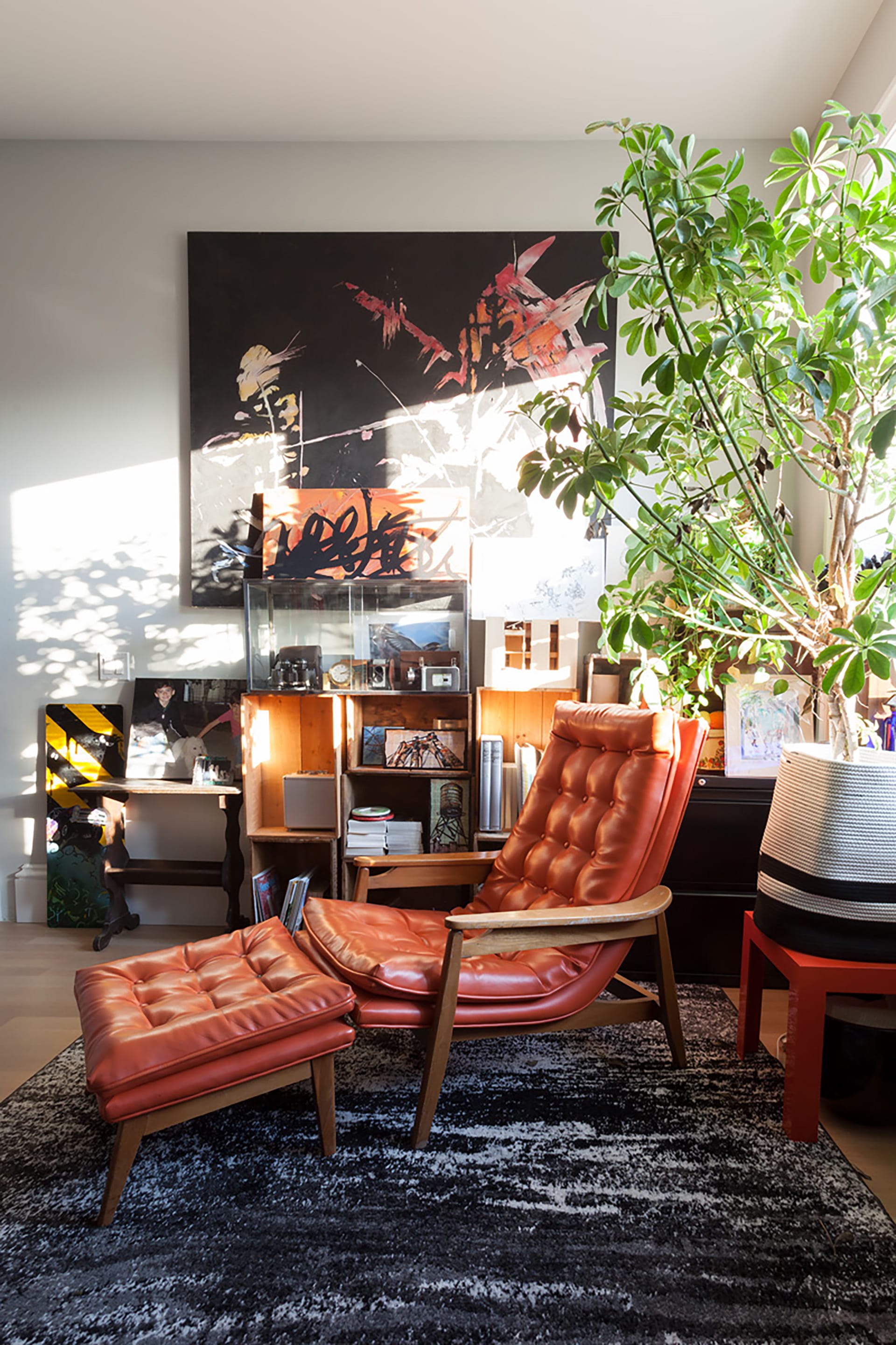 Office space in a Carroll Gardens Passive House with sunlight streaming through a window and a large potted plant. An orange leather lounge chair sits on a black and white carpet.