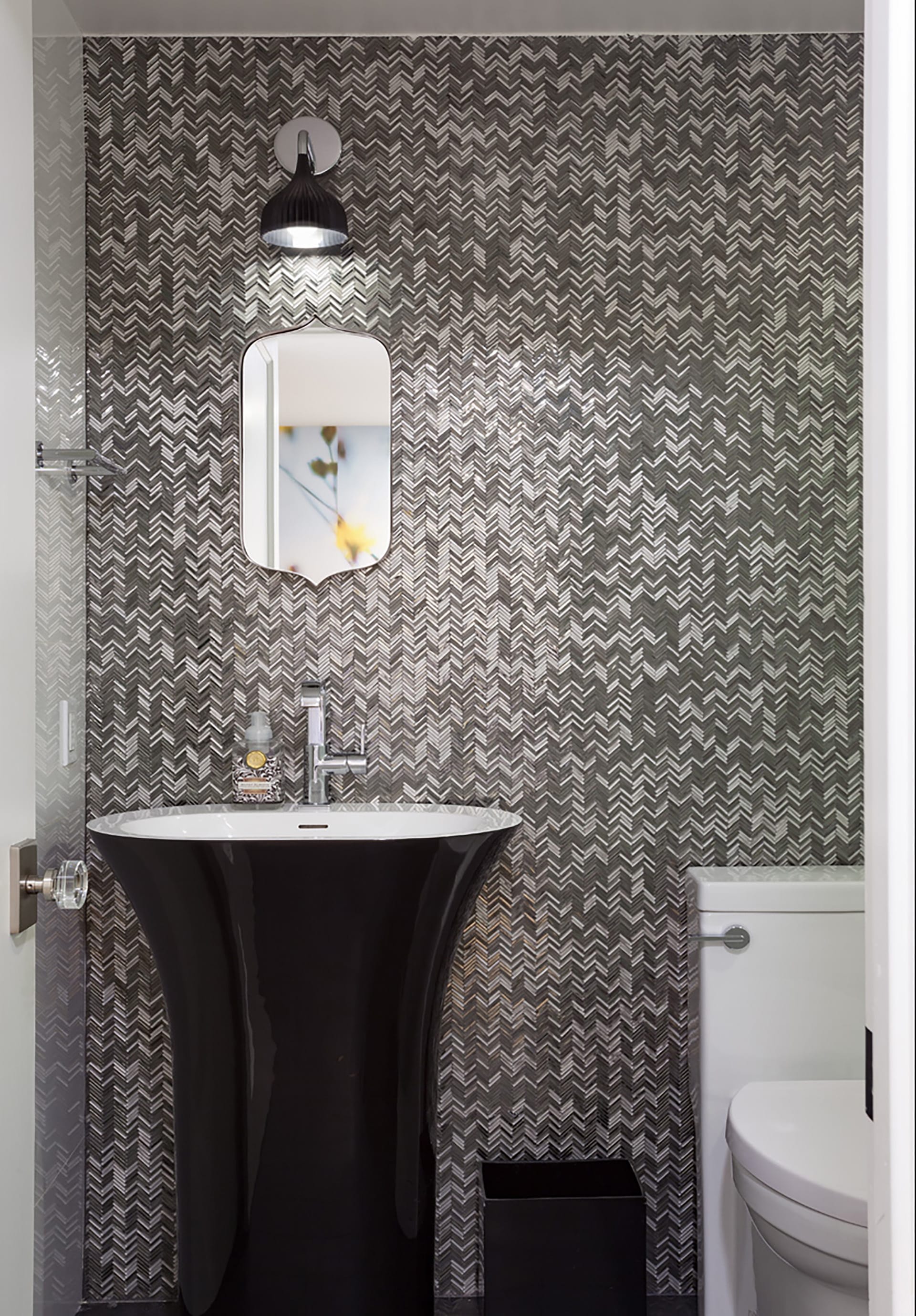 Powder room with grey and white mosaic-tiled walls and a black sink and sconce.