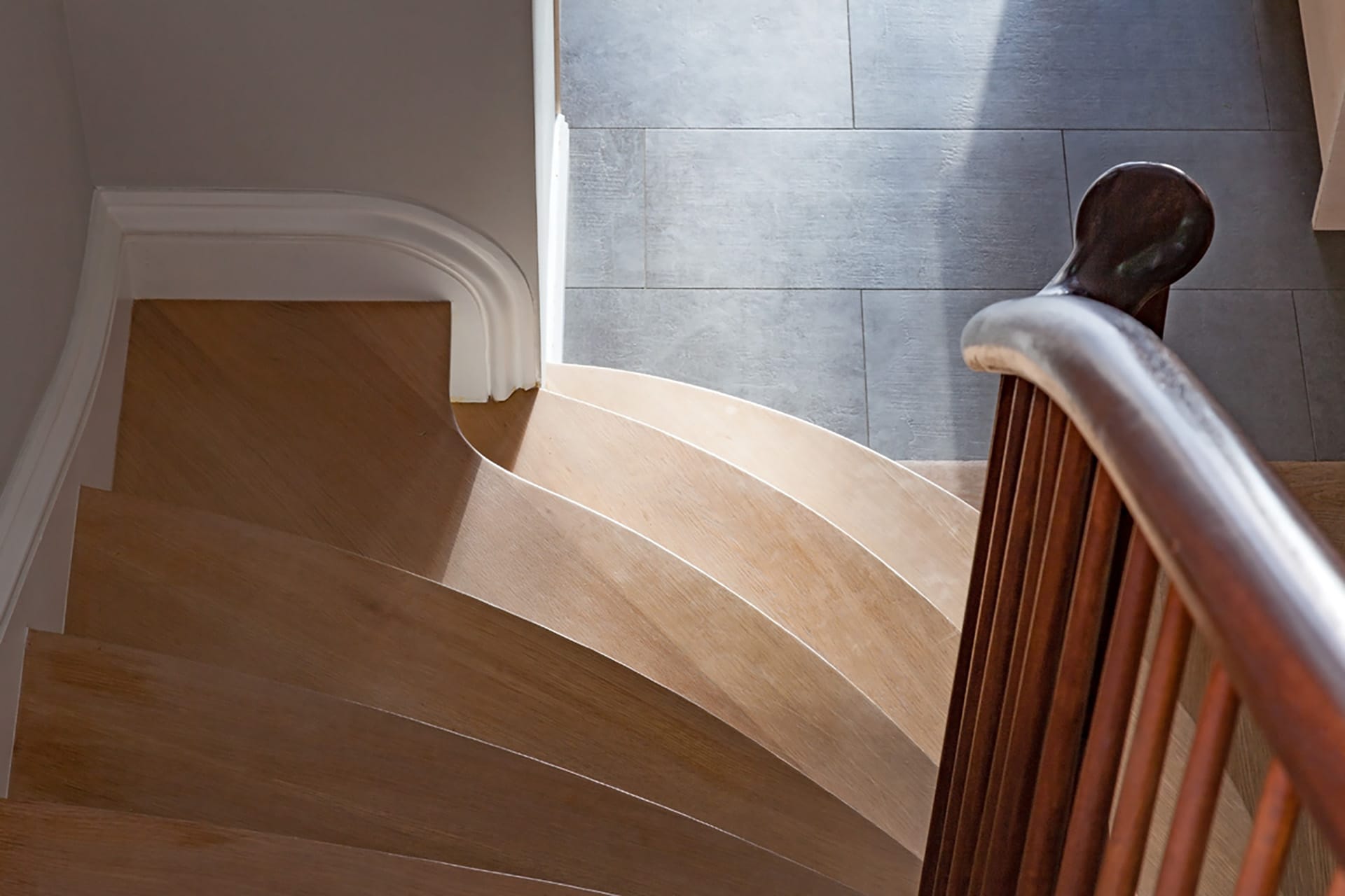 Stair landing with light wood risers, dark wood railings, and dark tile floors.