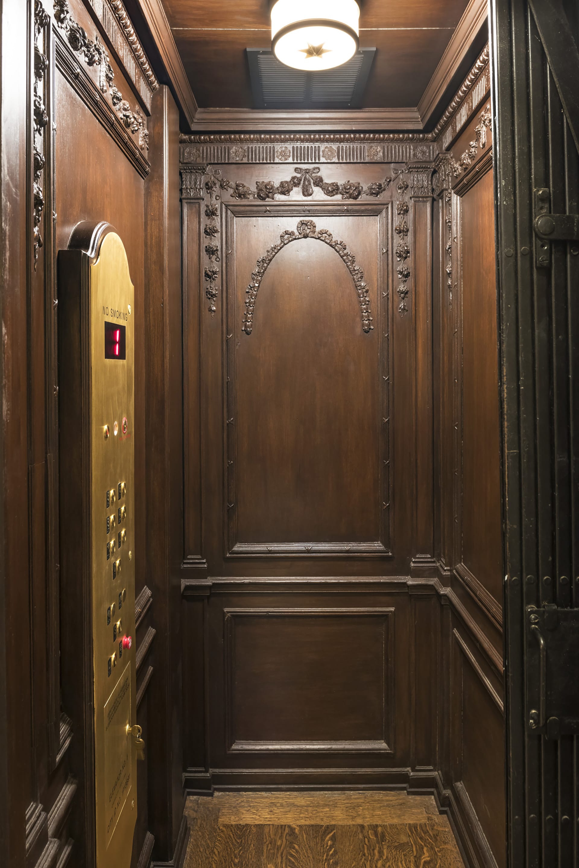 Restored elevator cab with carved wood walls and a gold control panel.