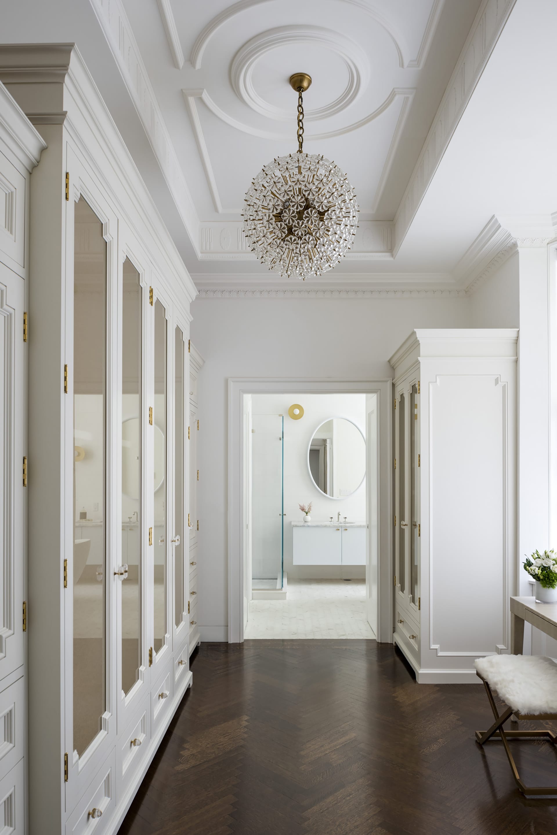 Closet with white millwork and a large, round chandelier in a primary bedroom.