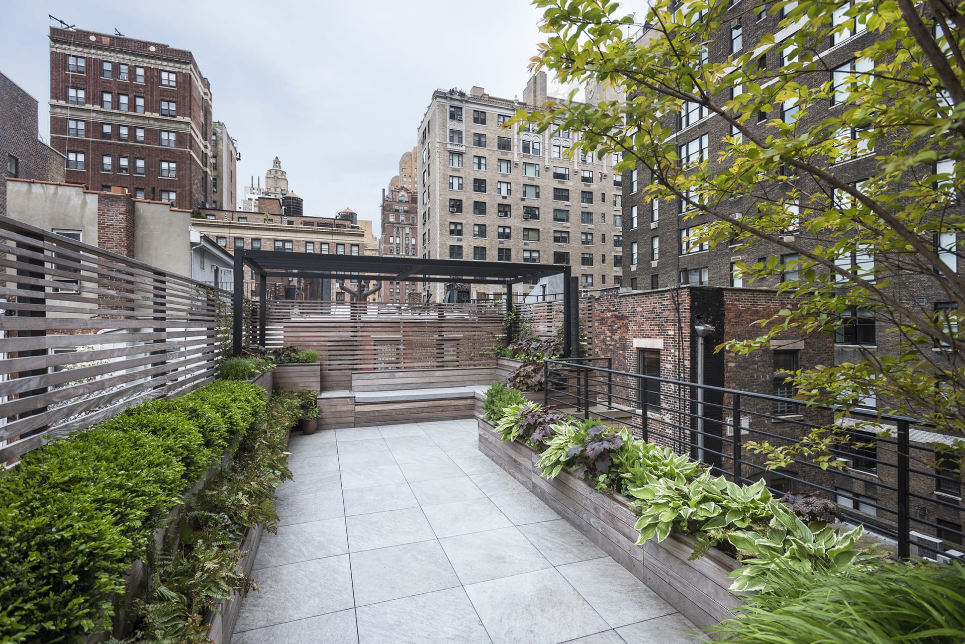 Roof deck with plantings, bluestone pavers, and a pergola on the Upper West Side of Manhattan.