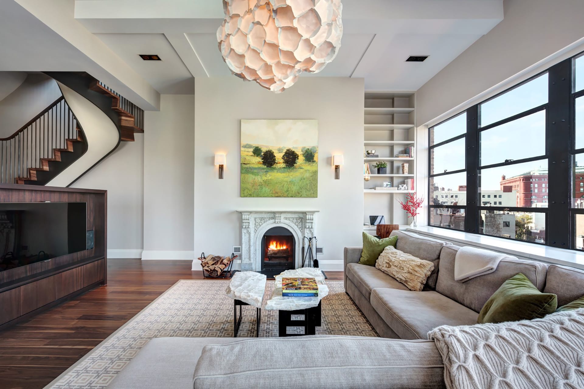 Living room with a large, artful chandelier, white fireplace, and sculptural stair in a West Village penthouse