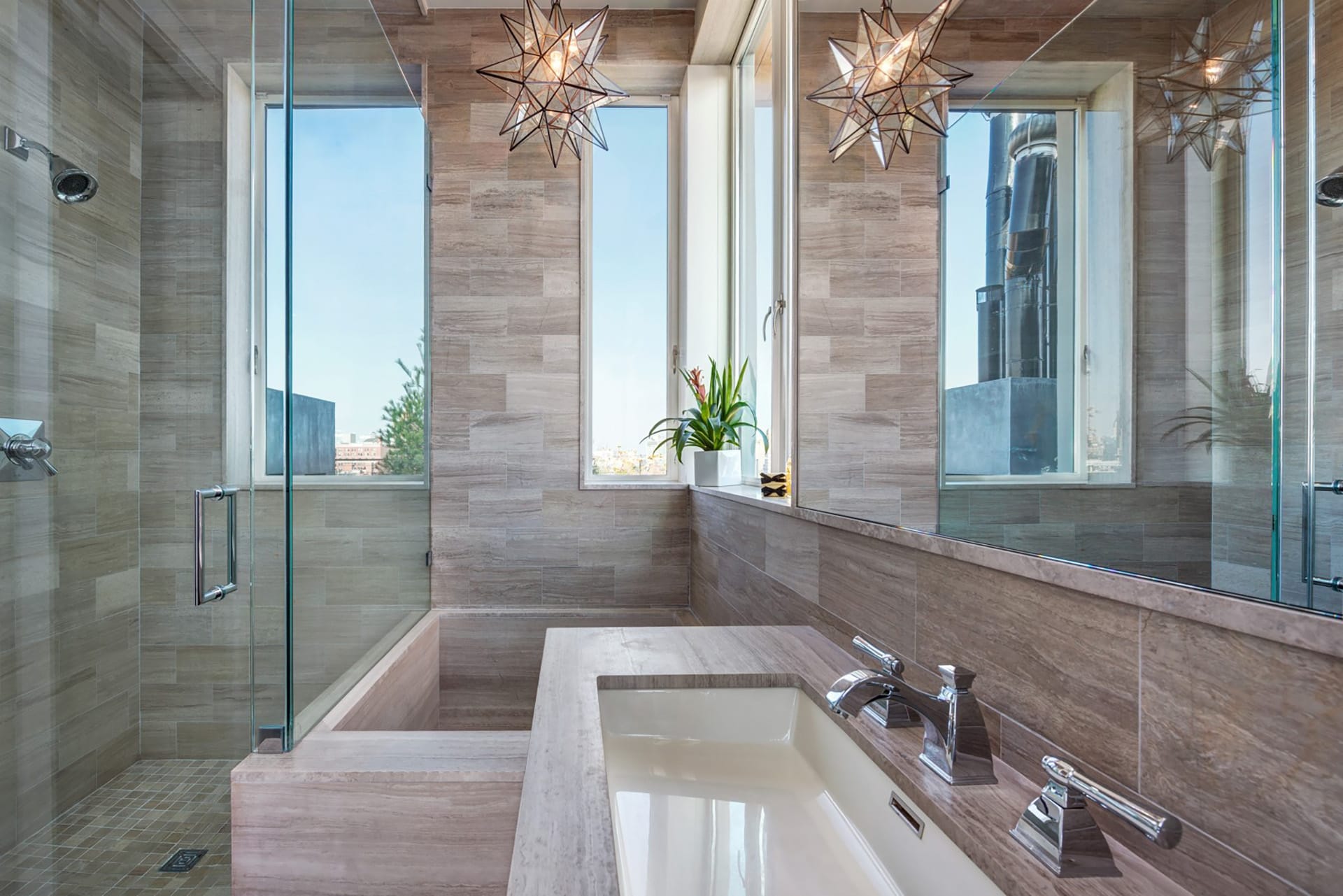 Primary bath with a geometric light fixture and stone covering the walls, floors, tub, and vanity.