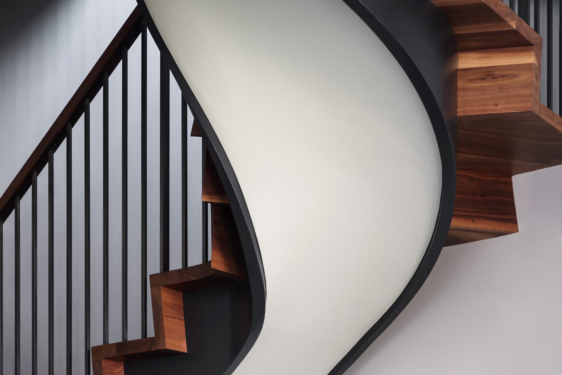 Sculptural staircase with black handrail and balusters, wood risers, and a white underside.
