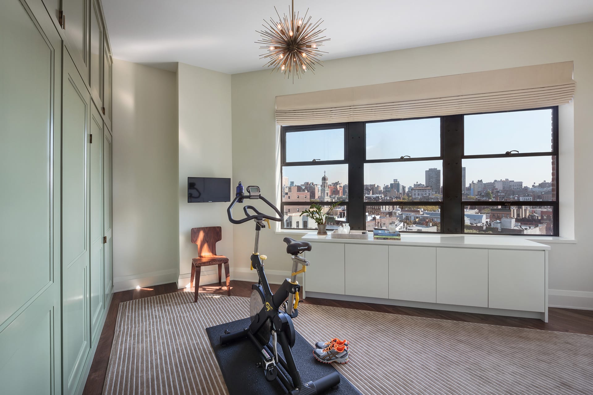 Triangular guest bedroom with a custom fitted area rug, exercise equipment, and Murphy bed tucked in to a wall covered with light green millwork.