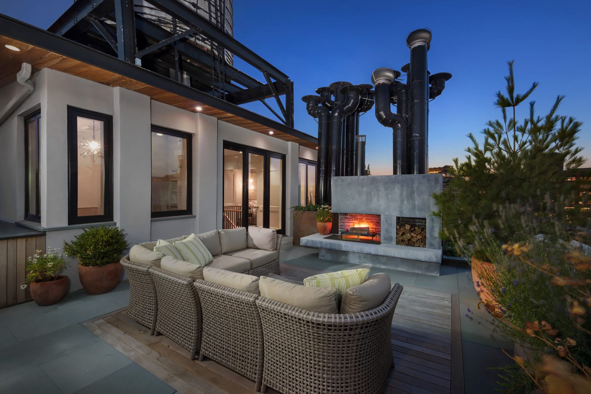 Roof deck with an outdoor seating area, kitchen, and wood-burning fireplace at twilight.