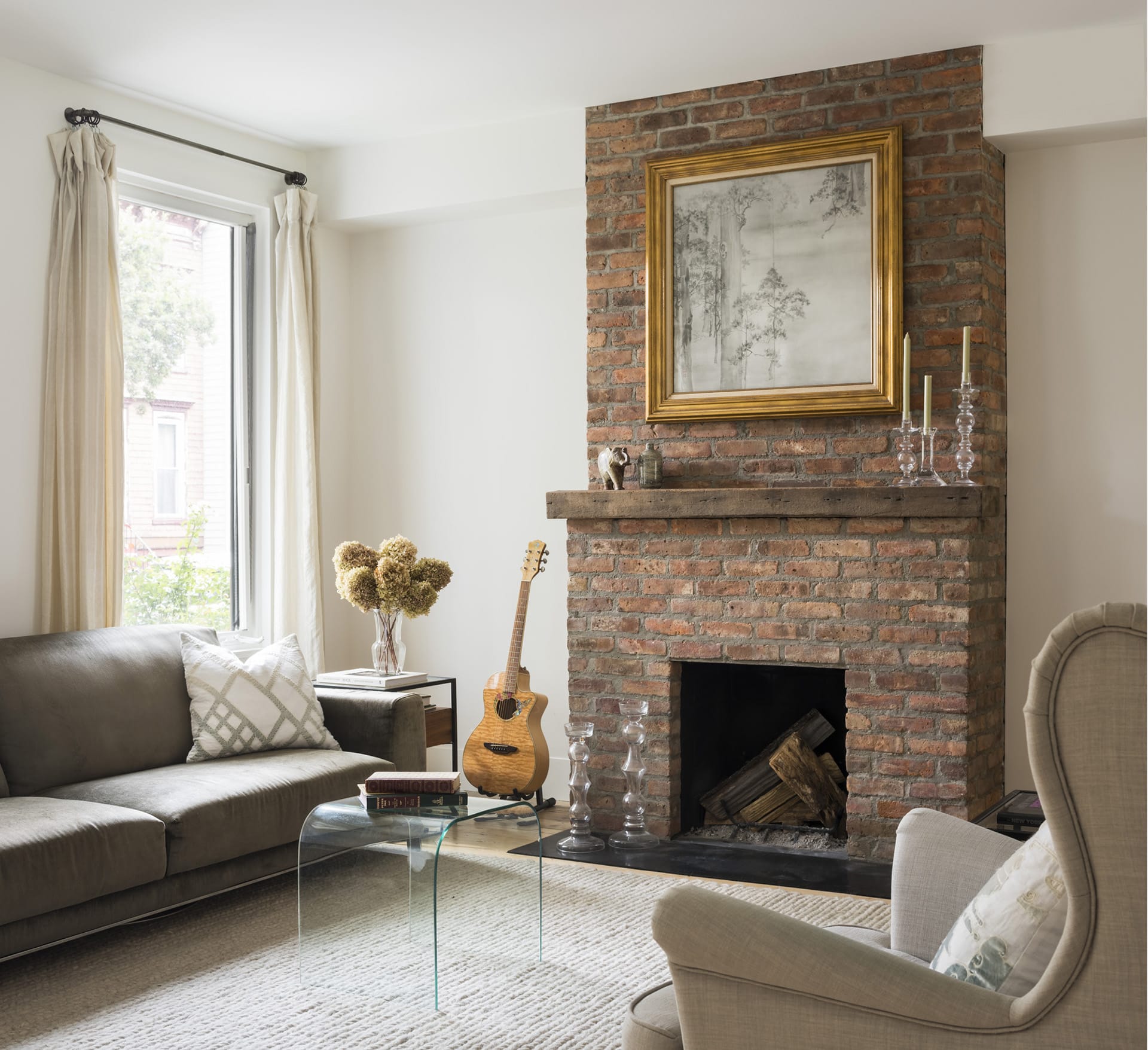 Living room in a Greenpoint townhouse with large brick fireplace, acoustic guitar, carpeted floors, and large window