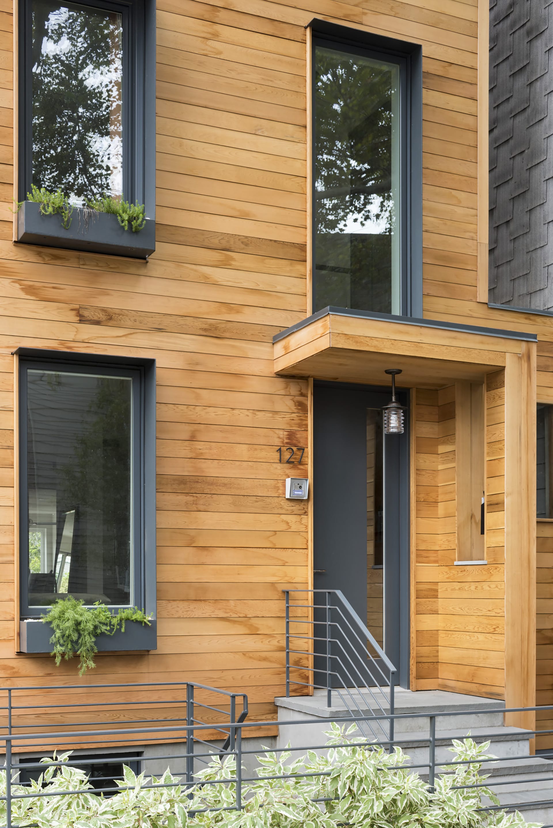 Exterior of a wood-framed Greenpoint townhouse with cedar siding, planters in front of the home and windows, and black window and door openings.