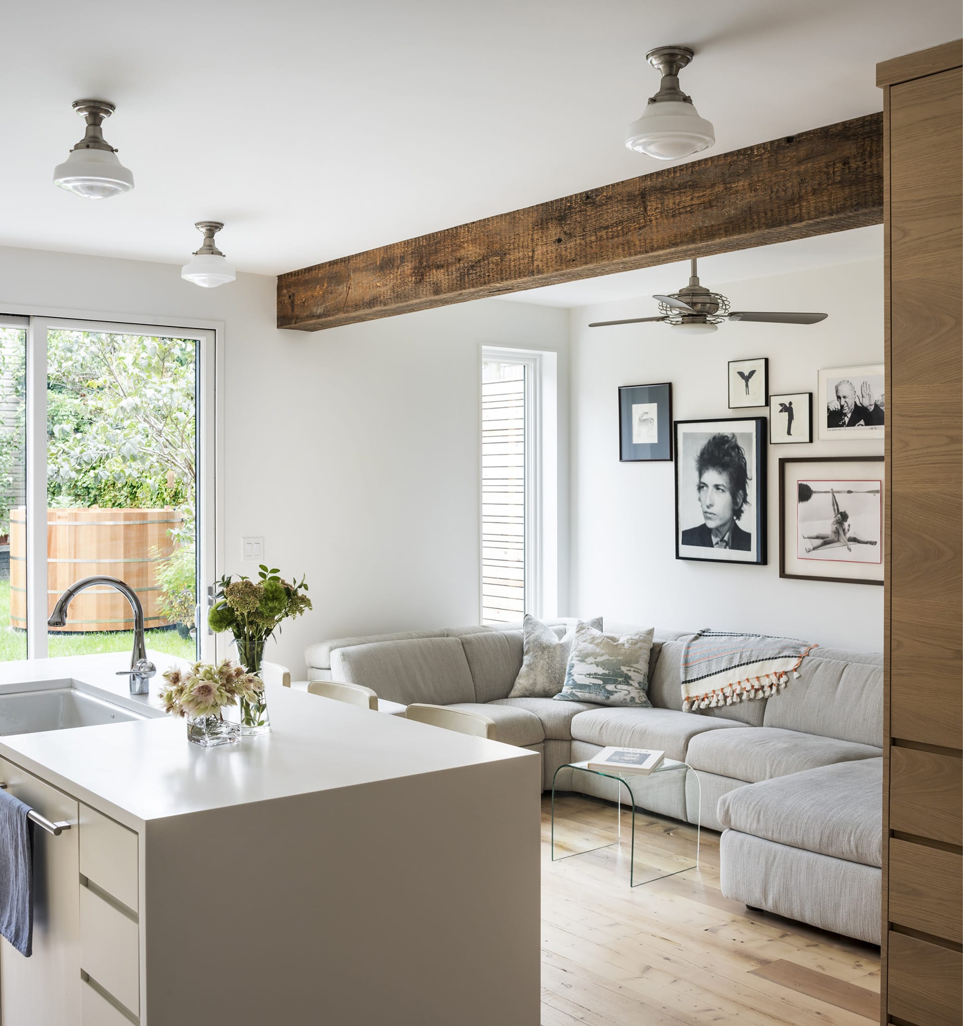 Kitchen island, exposed beam, and seating area with a grey sectional and gallery wall in a Greenpoint townhouse.