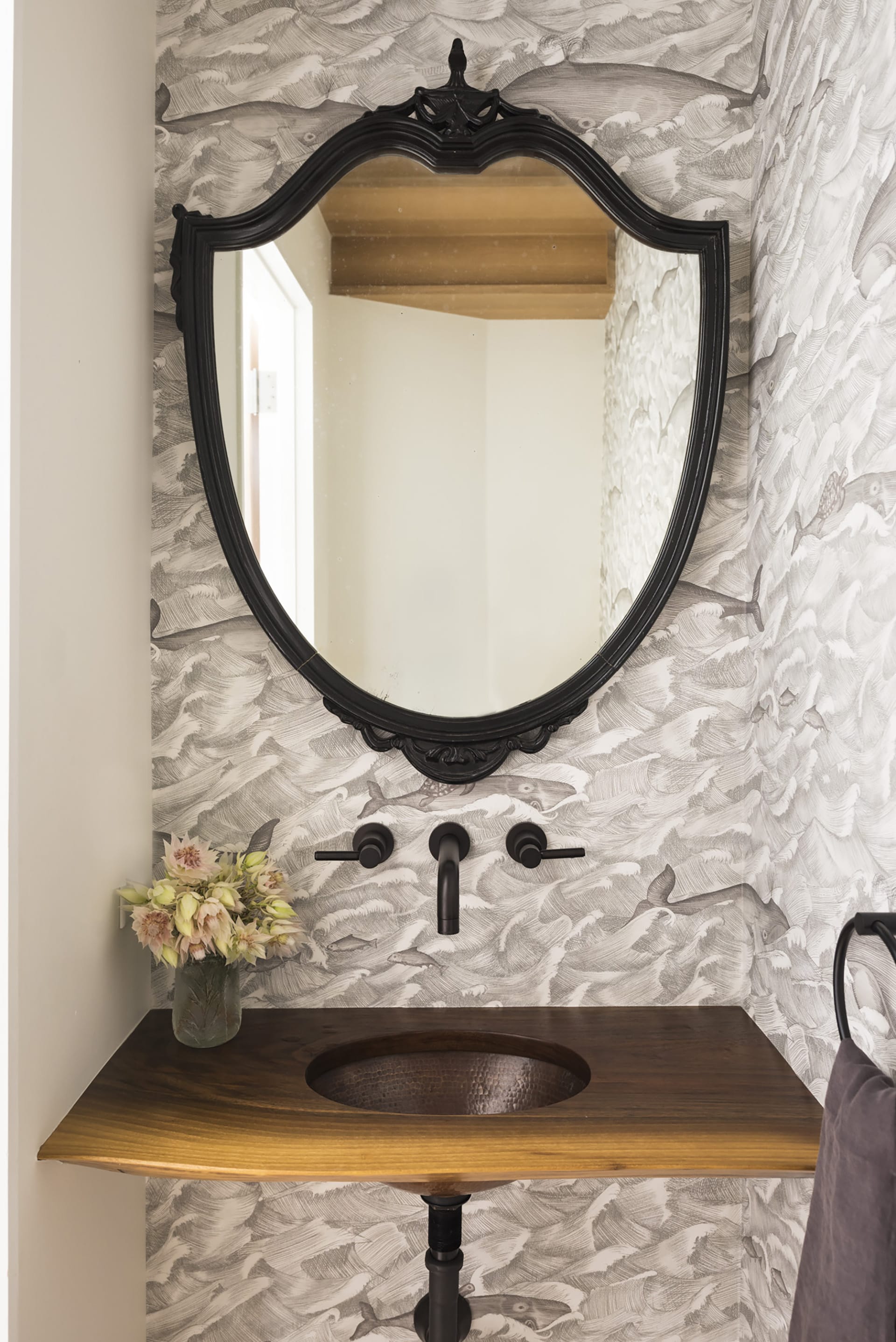 Sink and mirror in an under-staircase powder room with black and white whale wallpaper