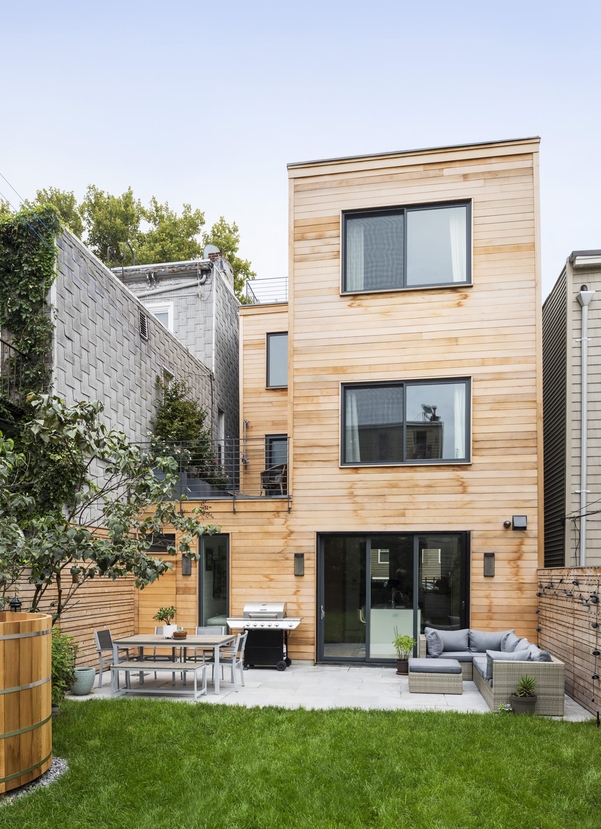 Exterior of a wood-framed Greenpoint townhouse with cedar siding, rear yard, and black window and door openings.