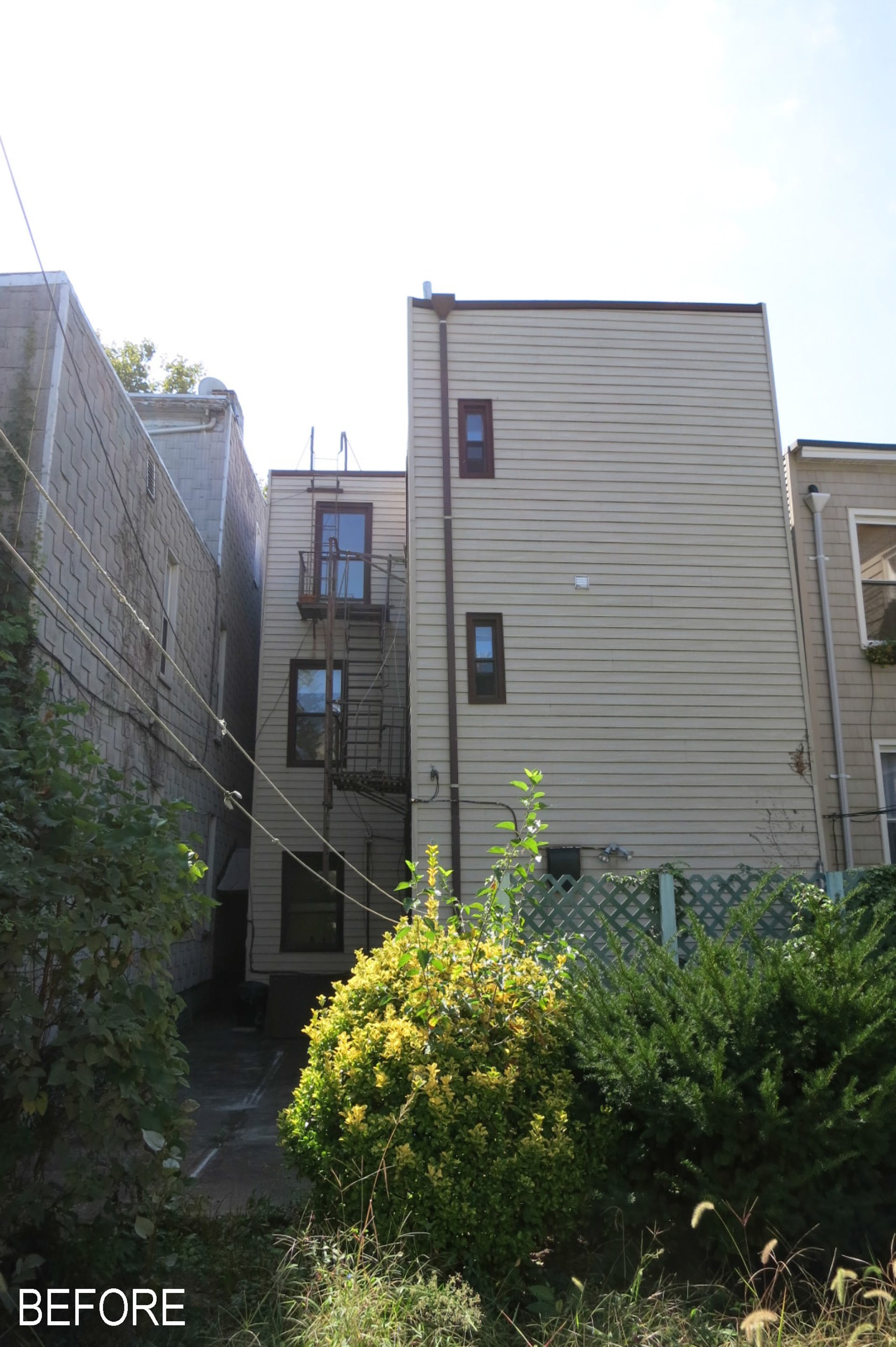 Greenpoint townhouse before our renovation, with white siding and dark window and door openings