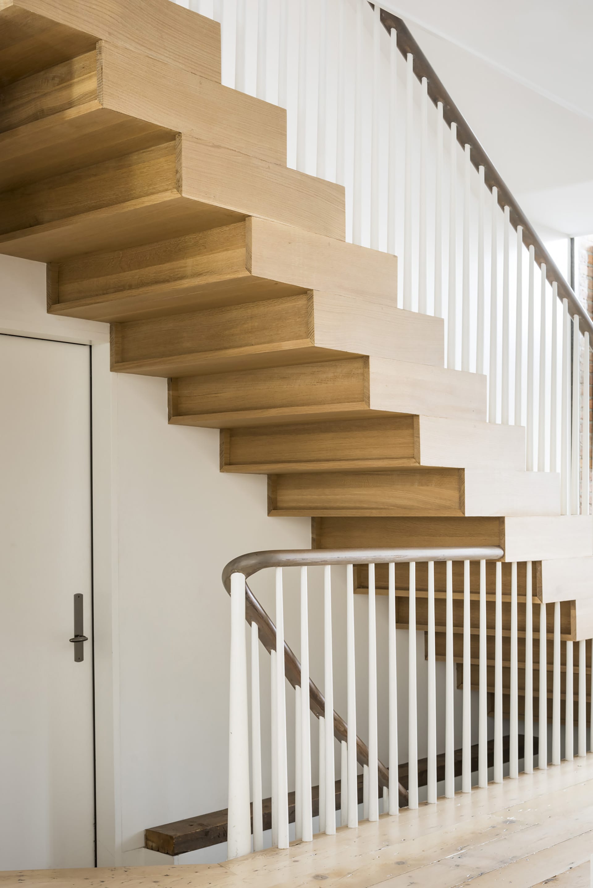 Staircase with stacked wood risers, white spindles, and a dark wood handrail.